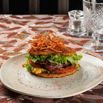 Дранбургер с говяжьей котлетой (сочная котлета между двумя фирменными драниками) с фирменным соусом, ломтиками свежего помидора, маринованных огурца и лука от Ресторана «Кухмистр»