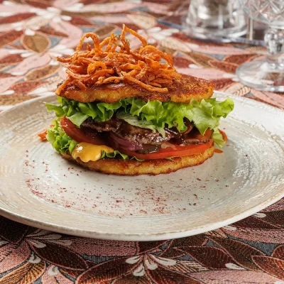 Дранбургер с говяжьей котлетой (сочная котлета между двумя фирменными драниками) с фирменным соусом, ломтиками свежего помидора, маринованных огурца и лука от Ресторана «Кухмистр»